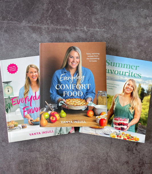 Three cookbooks by Vanya Insull are arranged in a fan-like layout on a dark textured surface. The center book is titled 'Everyday Comfort Food' and features a photo of the author holding a pie.